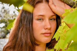 Artistic portrait with sunlit green leaves creating natural bokeh effects.