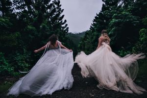 Dreamy forest photography with flowing white dresses among tall pine trees.