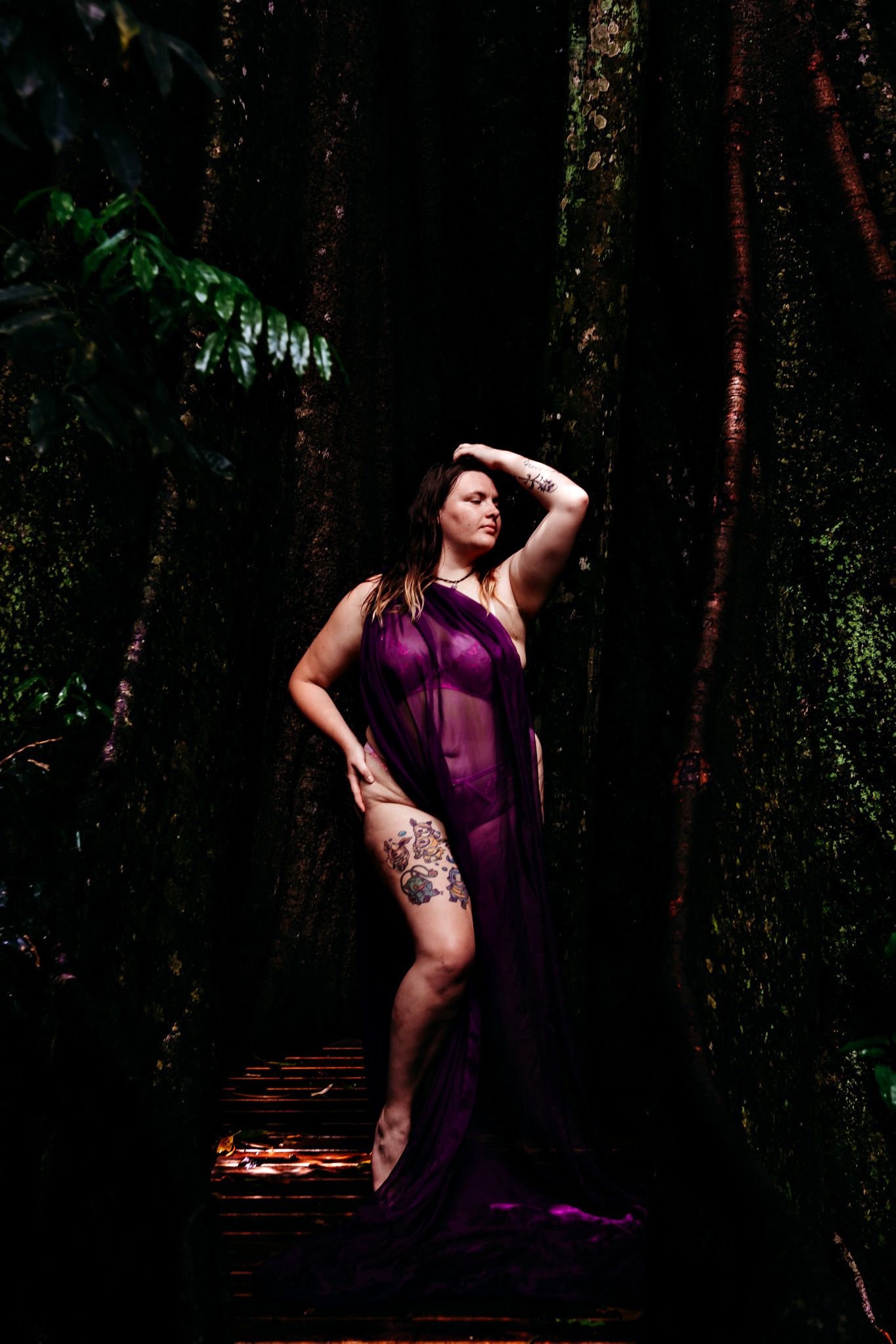 Artistic portraits in purple dress against dark forest backdrop with dramatic lighting.