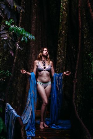Forest photoshoot with blue fabric draping in moody natural lighting.