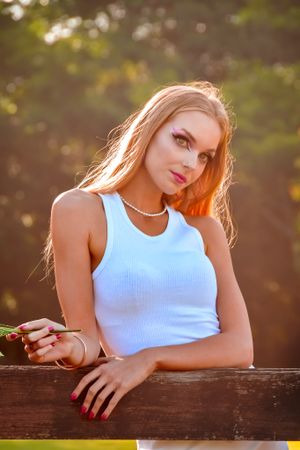 Artistic outdoor portrait in white tank top leaning on wooden fence during golden hour sunset.