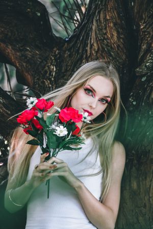 Ethereal portrait with red roses and white flowers against moody natural background.