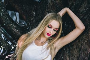 Dramatic fashion portrait with bold makeup against dark tree backdrop.