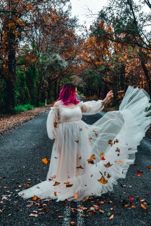 Ethereal portrait with flowing white fabric and autumn leaves scattered on a dark path.