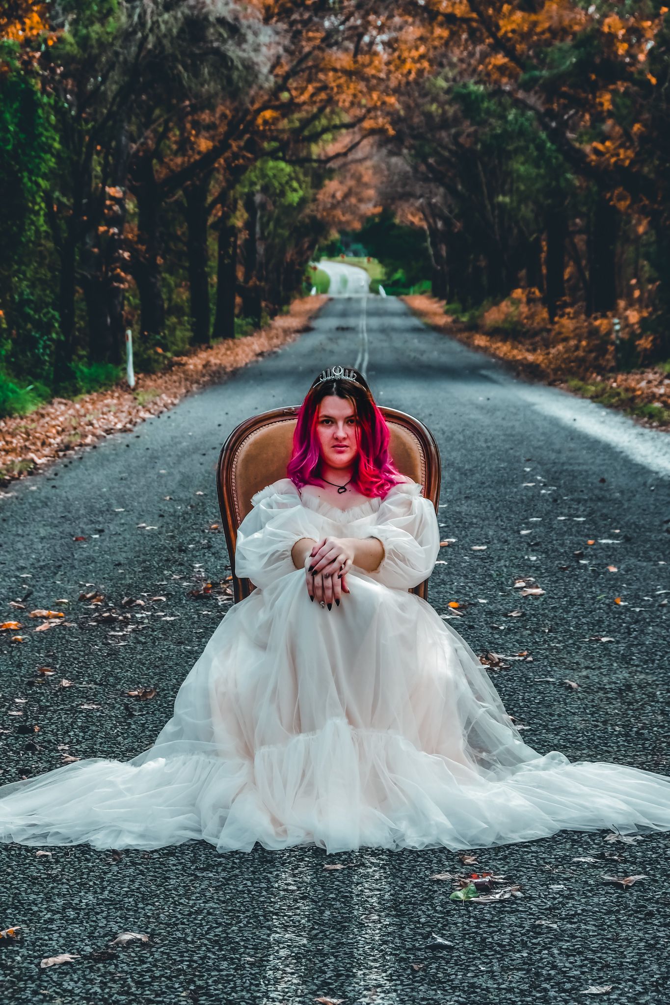 Dramatic fashion scene with a white gown and pink hair against a leaf-covered forest road.