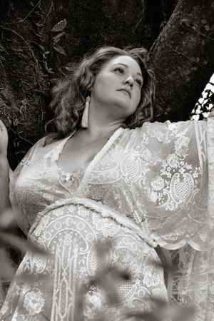 Black and white artistic portrait against a tree trunk wearing lace.