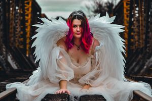 Artistic portrait with white feathered wings and flowing dress in an autumn forest setting.