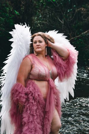Dramatic portrait with pink tulle dress and white angel wings by a lake.