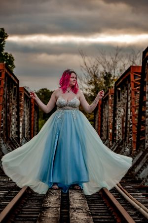 Dreamy portrait in a blue and white gown posed on rustic railroad tracks at sunset.