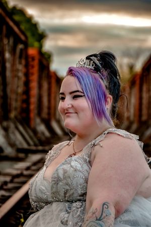 Artistic portrait with silver dress and purple hair against rustic industrial backdrop.