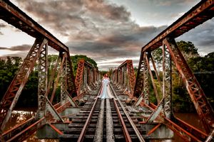 Wide angle view of a rustic railroad bridge with dramatic sunset clouds.