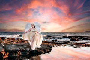 Ethereal beach photography with flowing white dress against dramatic sunset sky.