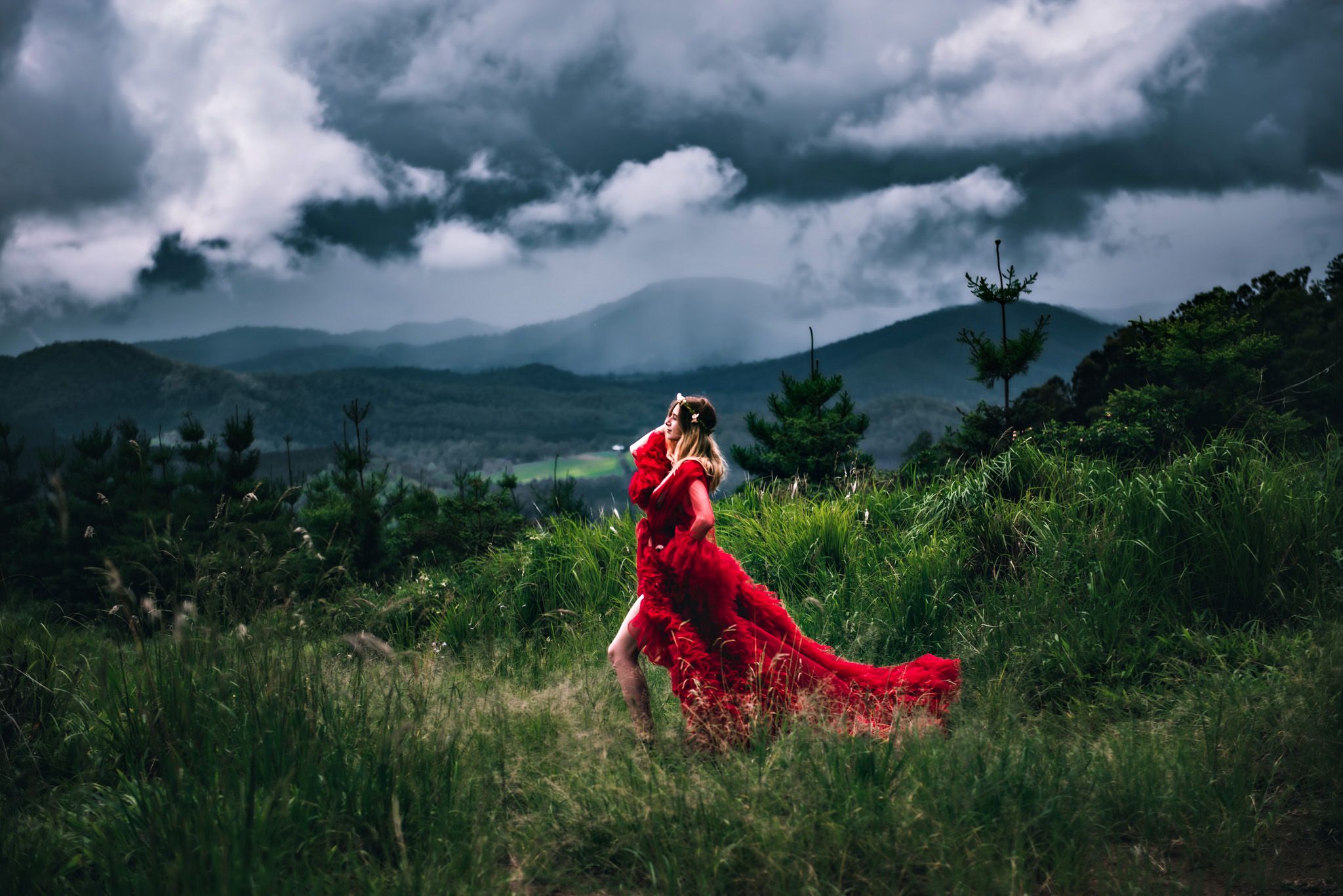 Dramatic landscape with red dress flowing in mountain scenery under moody clouds.
