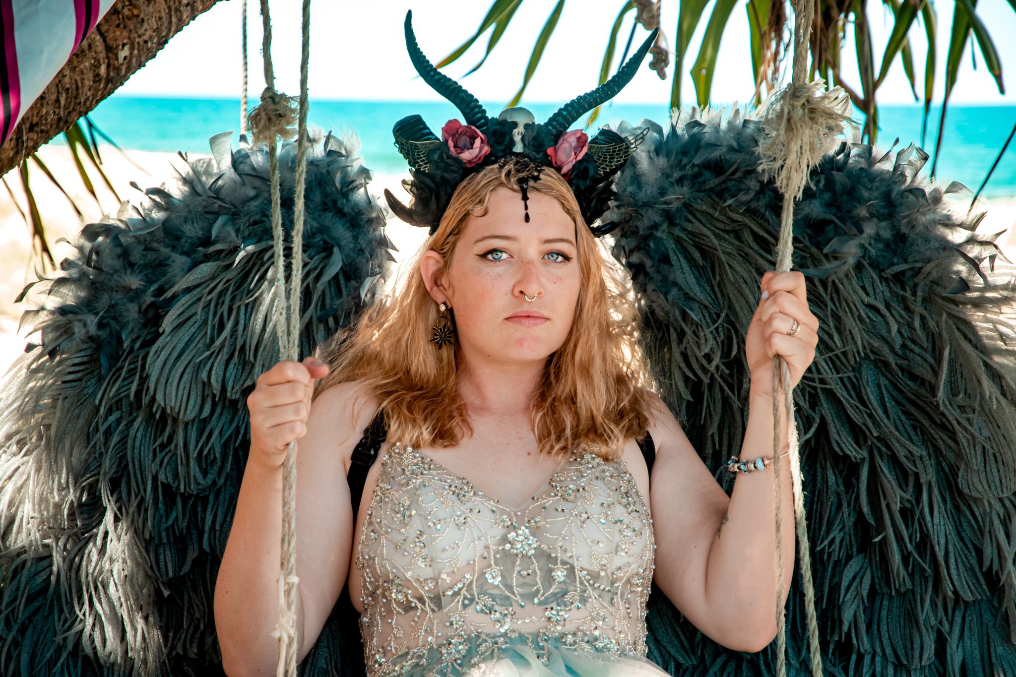 Beach photoshoot with dark feathered backdrop and turquoise ocean view.