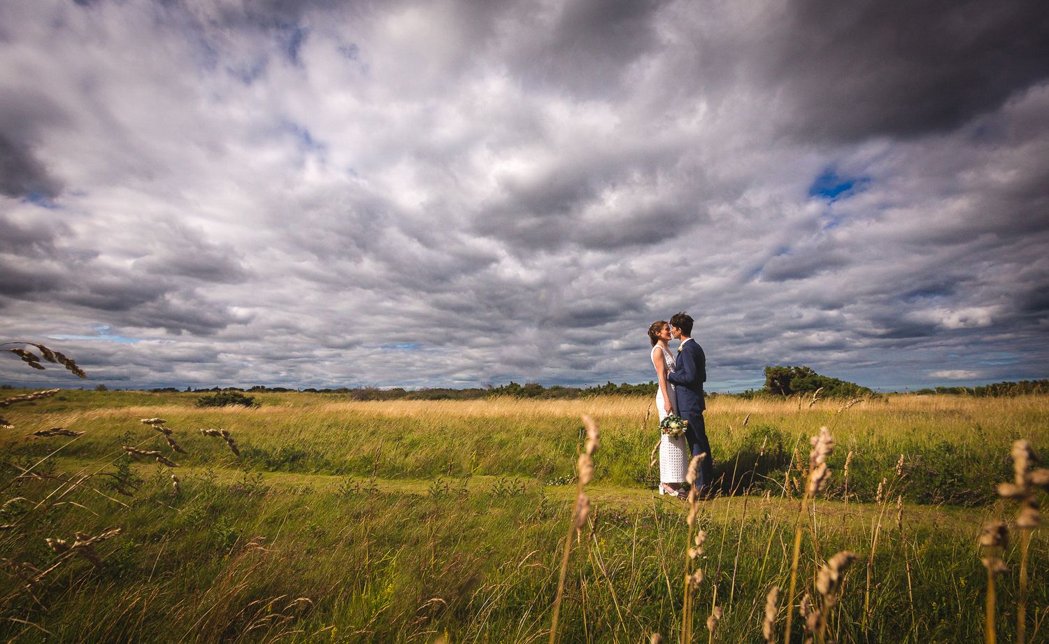 A figure stands in a grassy field under dramatic stormy clouds with patches of blue sky visible.