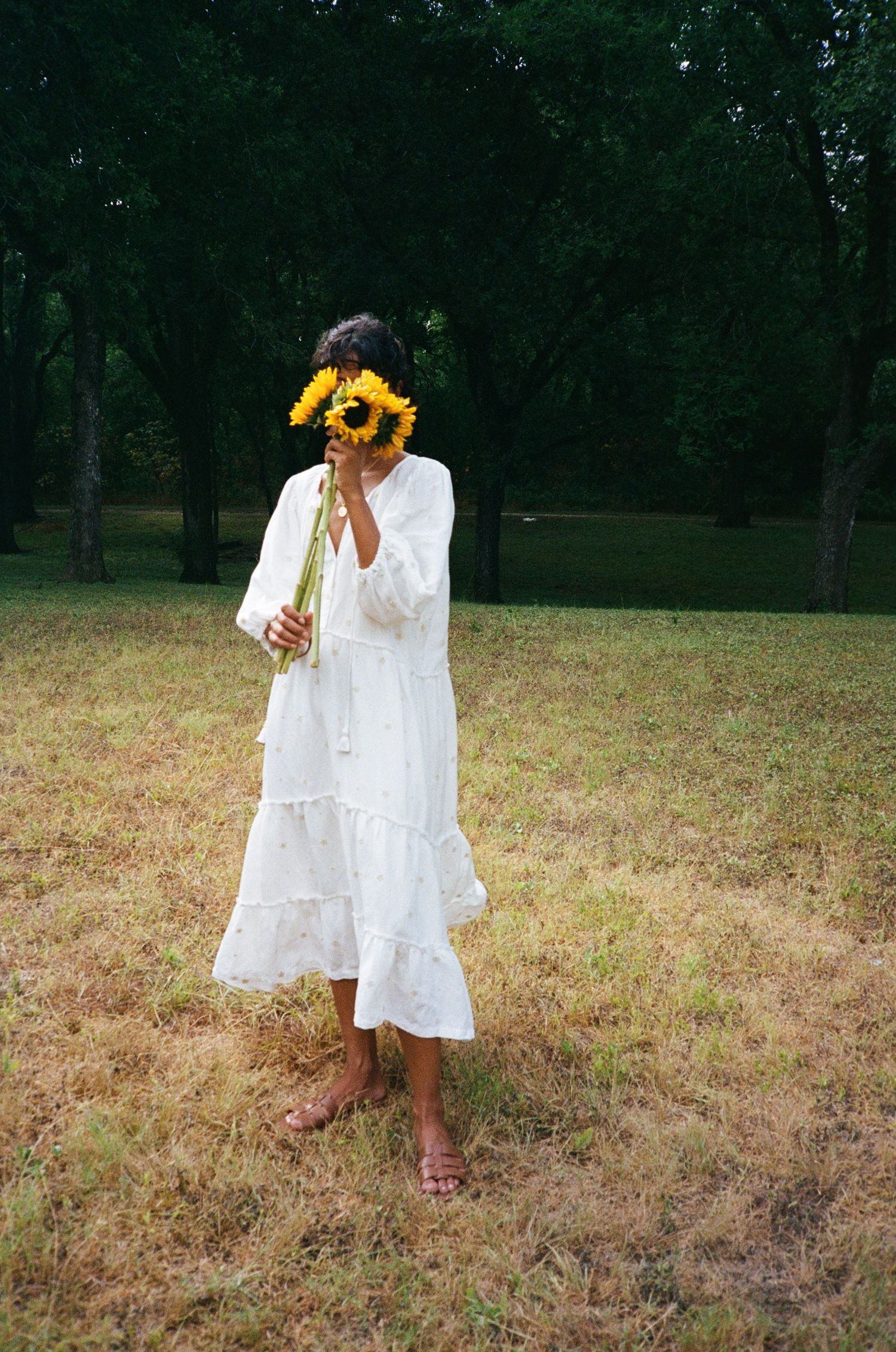 Sanetra Longno film photo of a woc holding sunflowers cover their face wearing a white Harper & Sage dress