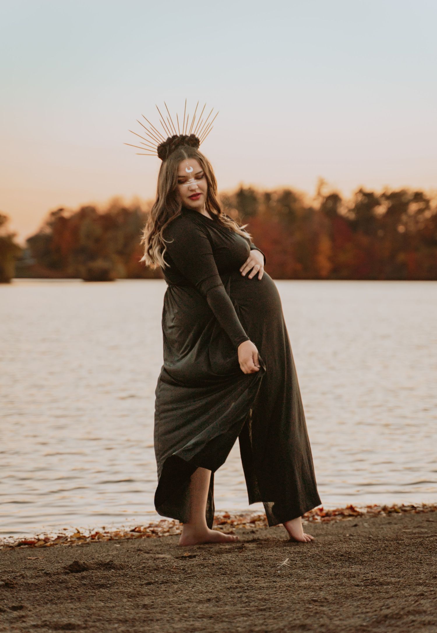 Woman holding her belly in front of water.