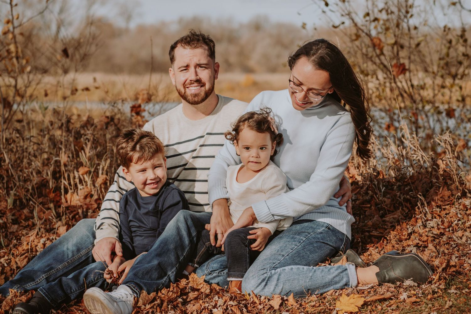 Image of family sitting in leaves in front of water.