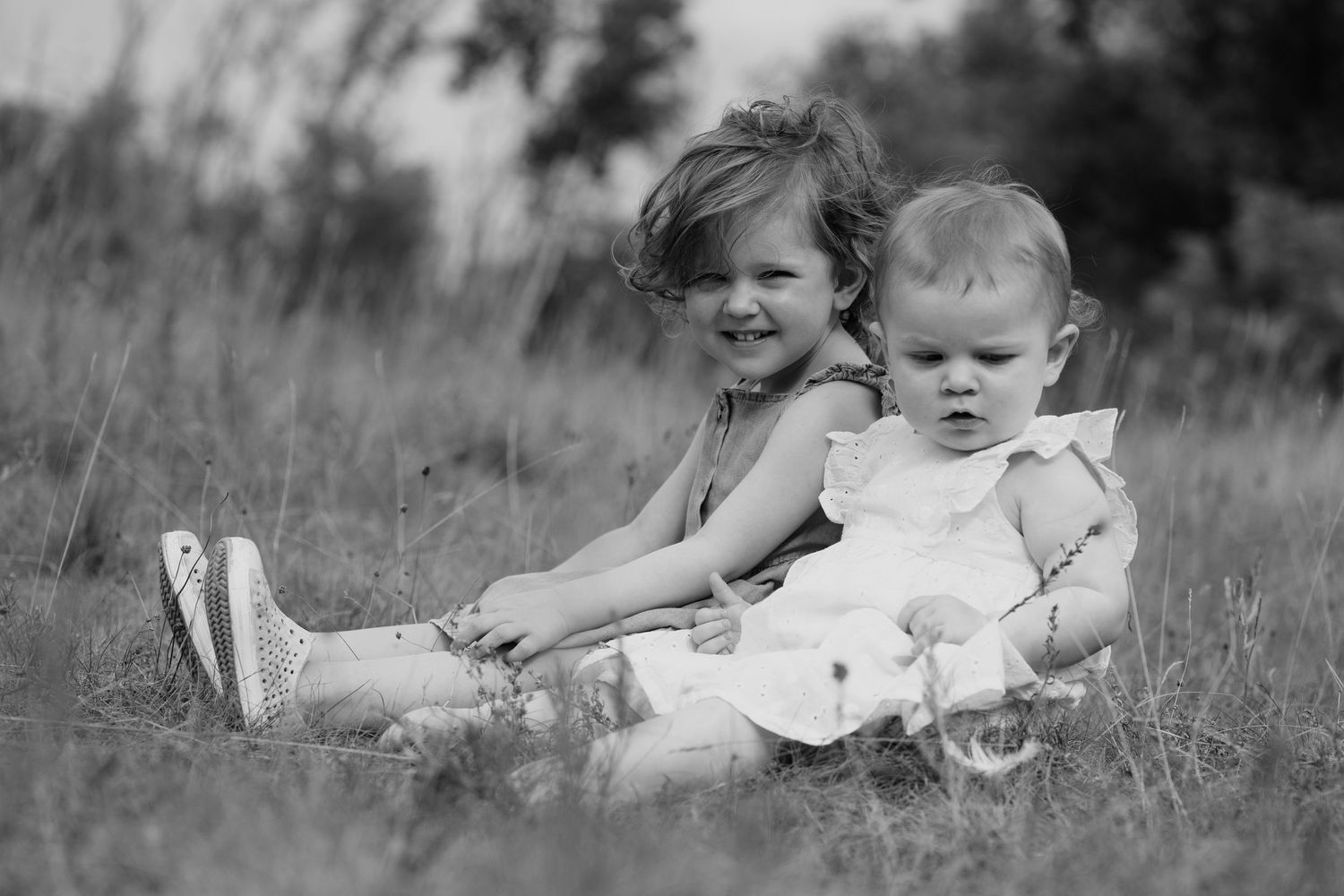 Black and white image of young girls sitting in field.