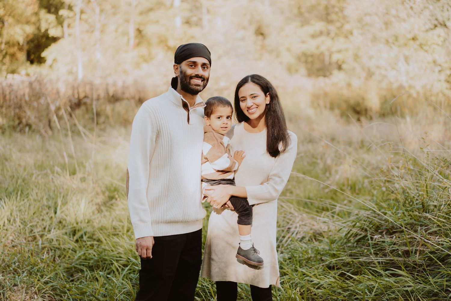 Image of family of three smiling in field.
