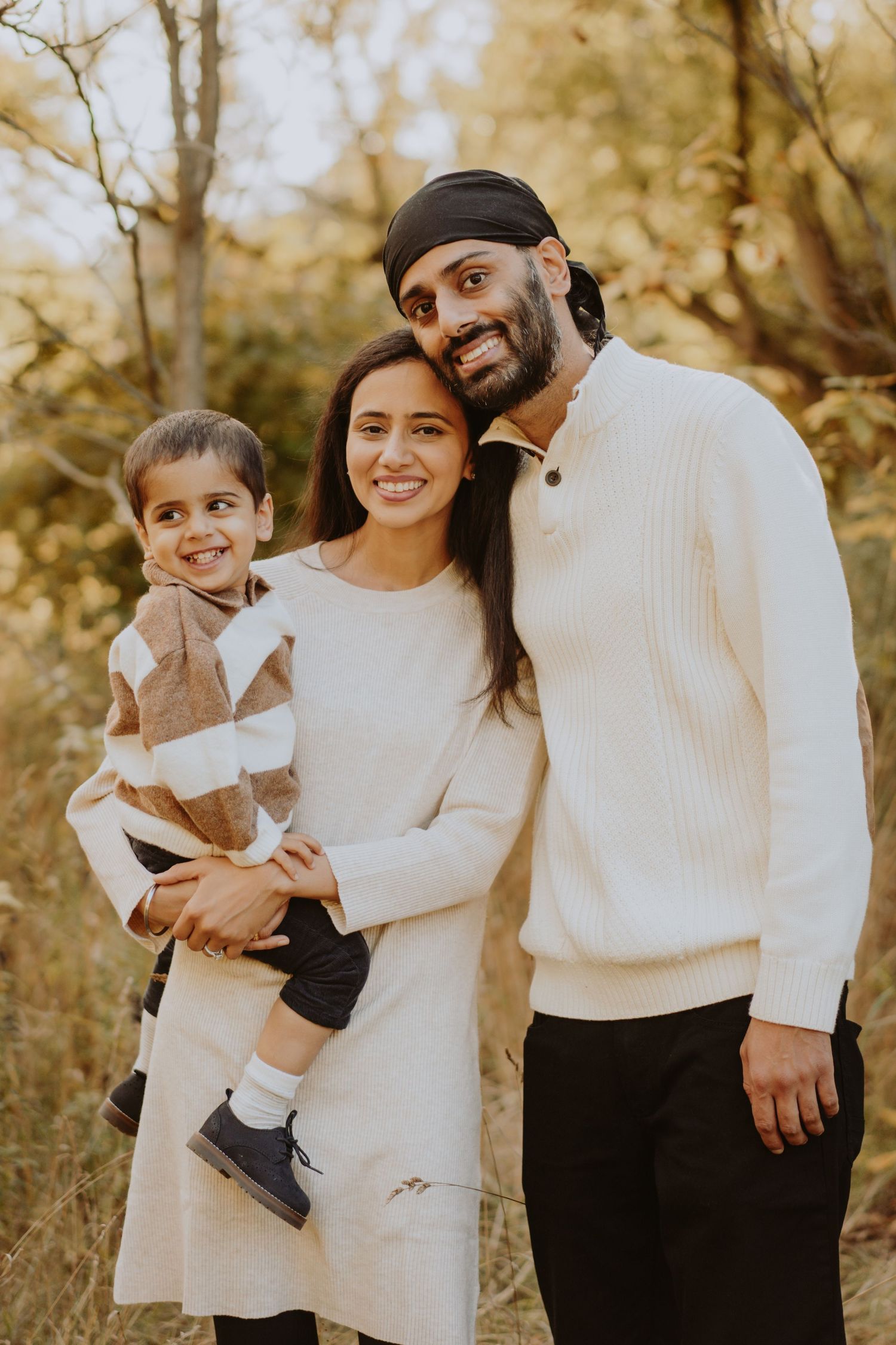 Image of family of three smiling in front of trees.