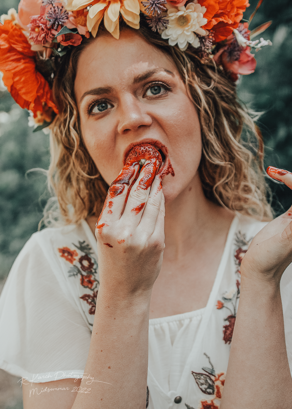 Playful moment captured eating strawberries while wearing floral embroidered dress and orange flower crown.