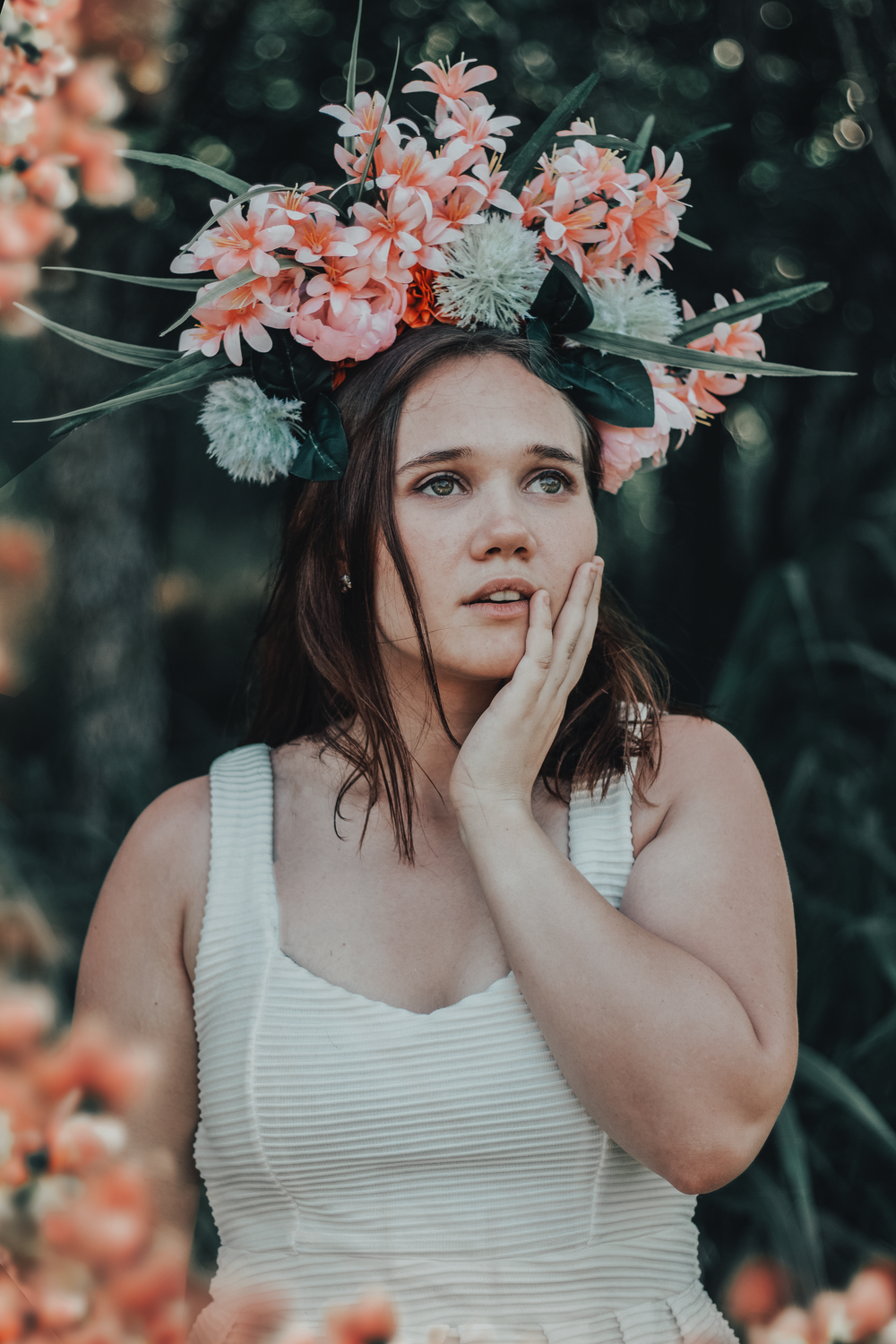 Dreamy summer portrait with coral and white flower crown in natural setting.