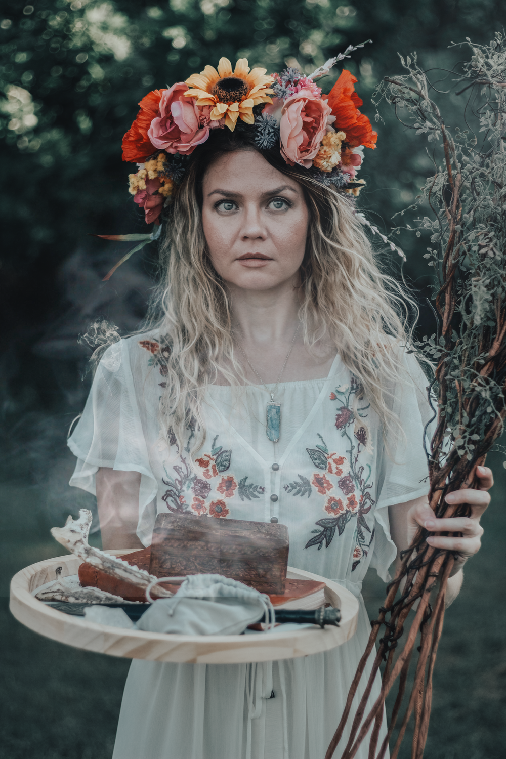 Moody forest portrait with floral crown holding vintage props and dried flowers.