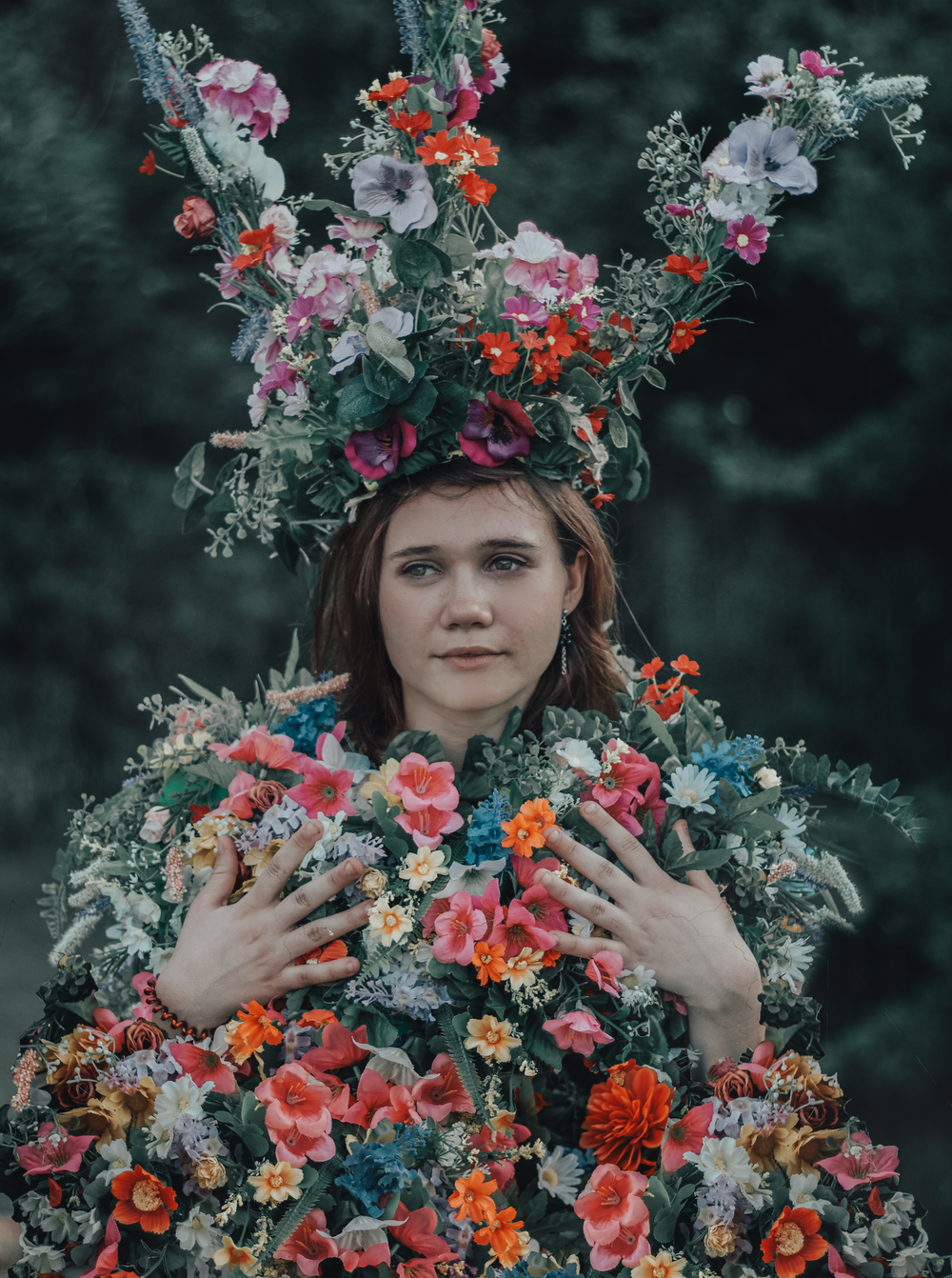 A dramatic portrait featuring an elaborate floral crown and dress made entirely of colorful blooms.