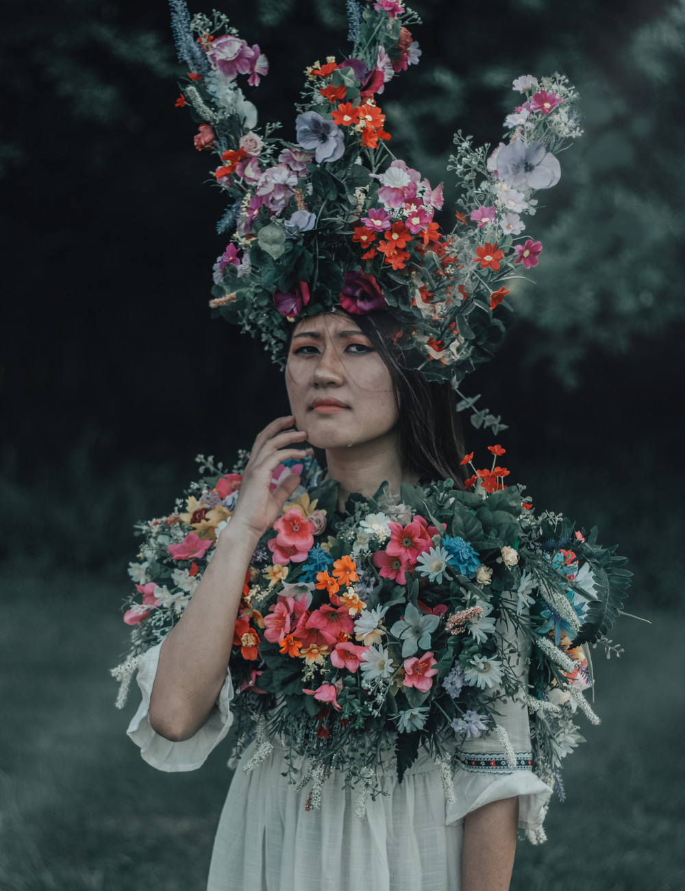 Ethereal portrait featuring elaborate floral crown with red and pink blooms.