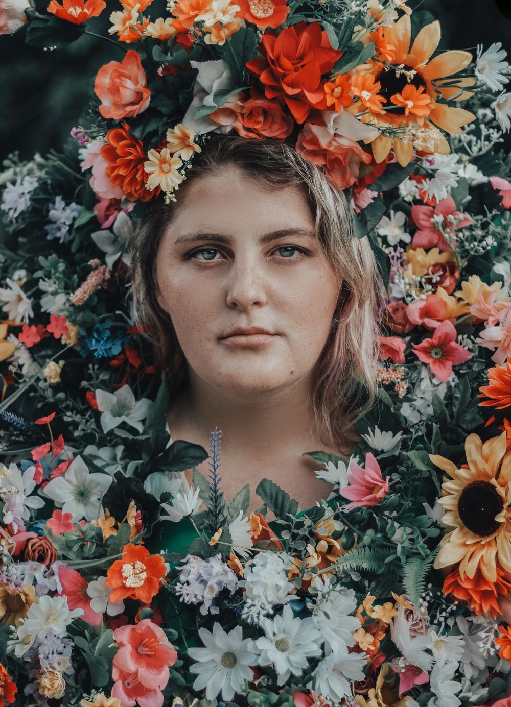 A portrait surrounded by vibrant orange and white flowers in a dramatic floral crown composition.