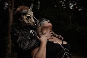 Dark fantasy themed photo with two masked figures in dramatic choking pose among trees.