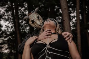 Intense close-up forest shot of two figures in masks with gothic styling.