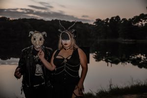 Moody lakeside portrait with animal masks and antlers against a dusky sunset.