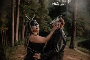 Dramatic forest portrait of two masked figures in dark clothing performing a dance-like pose.