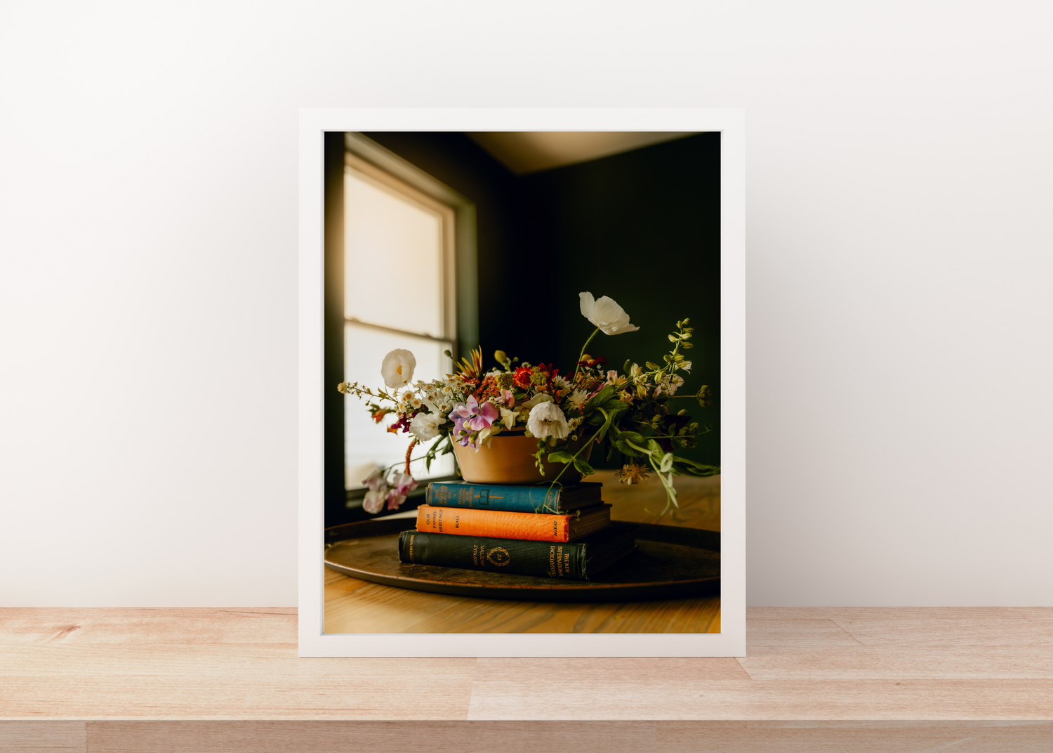 Still life composition with vintage books and floral arrangement by window in golden light.