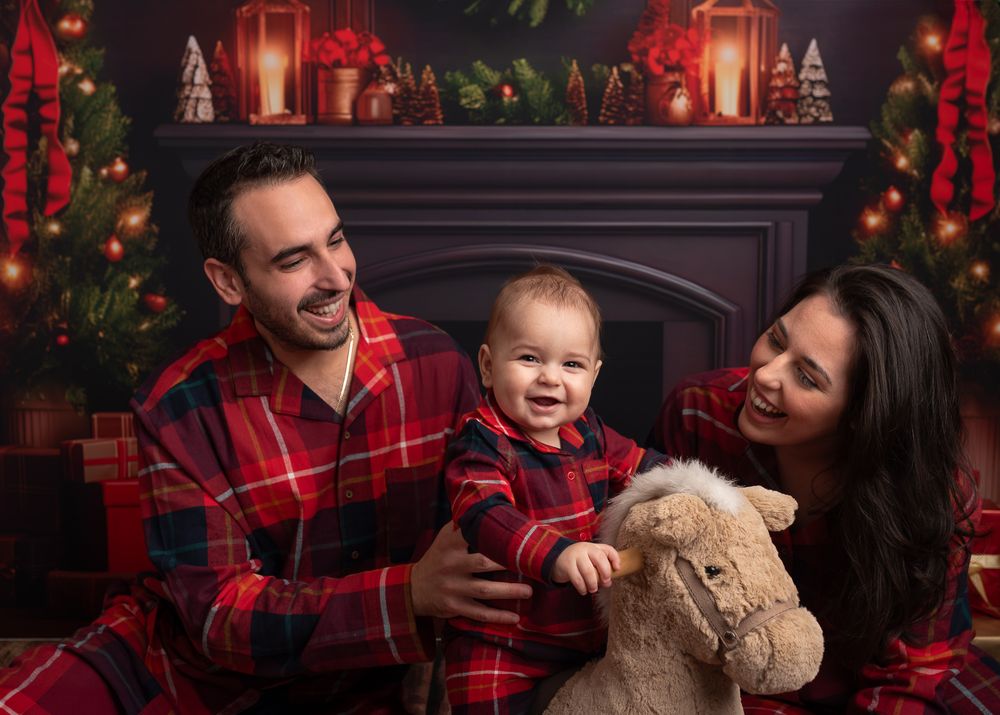 mum, dad and baby wearing Christmas pyjamas, fireplace, lantern, christmas tree. rocking horse