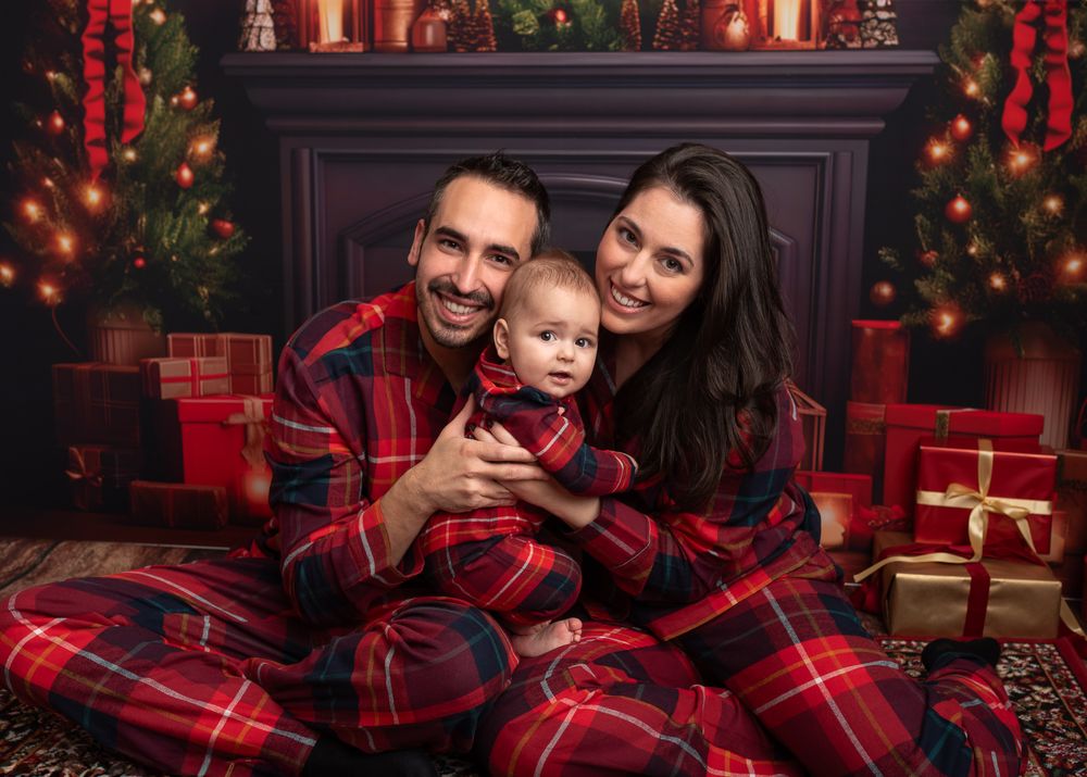 mum, dad and baby wearing Christmas pyjamas, fireplace, lantern, christmas tree.