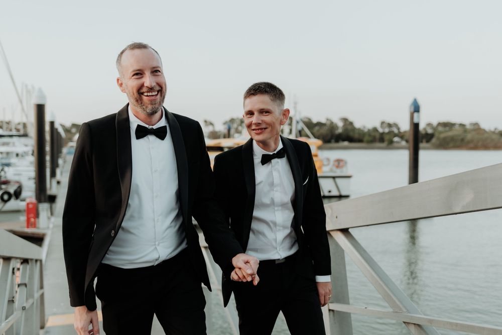 A happy couple in formal attire laughs together during their gladstone waterfront wedding photoshoot.
