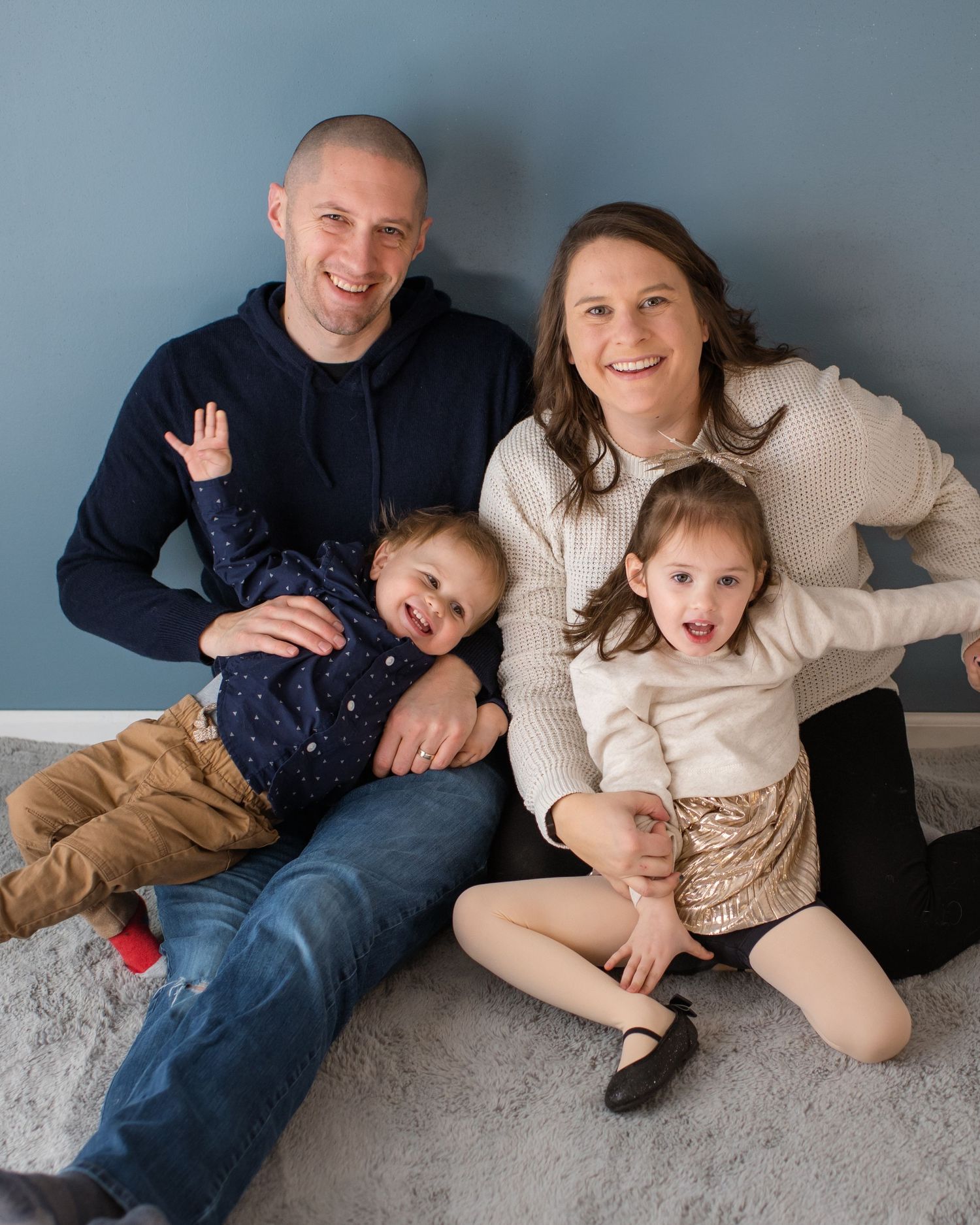 Family group sitting and posing together on grey carpet against blue wall.
