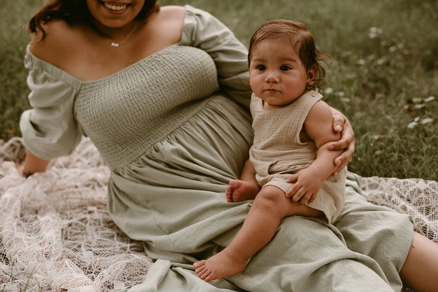 A tender moment between parent and baby sitting on white lace during an outdoor photo session.