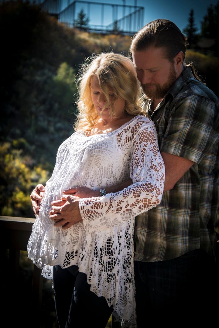Maternity photo with woman in lace and man in plaid wrapping his arms around her