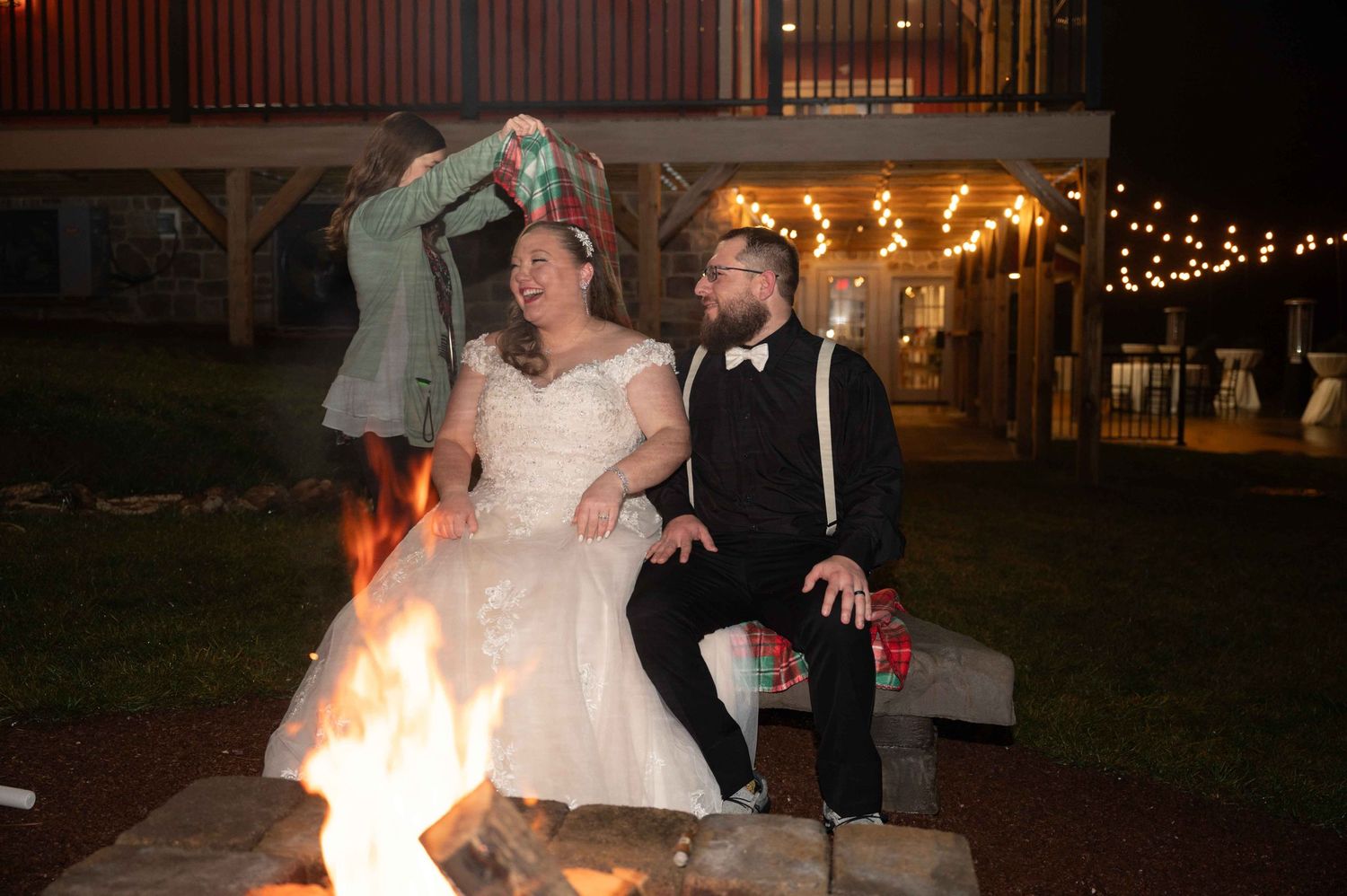 Newlyweds sit by a glowing fire pit at night during their wedding celebration.