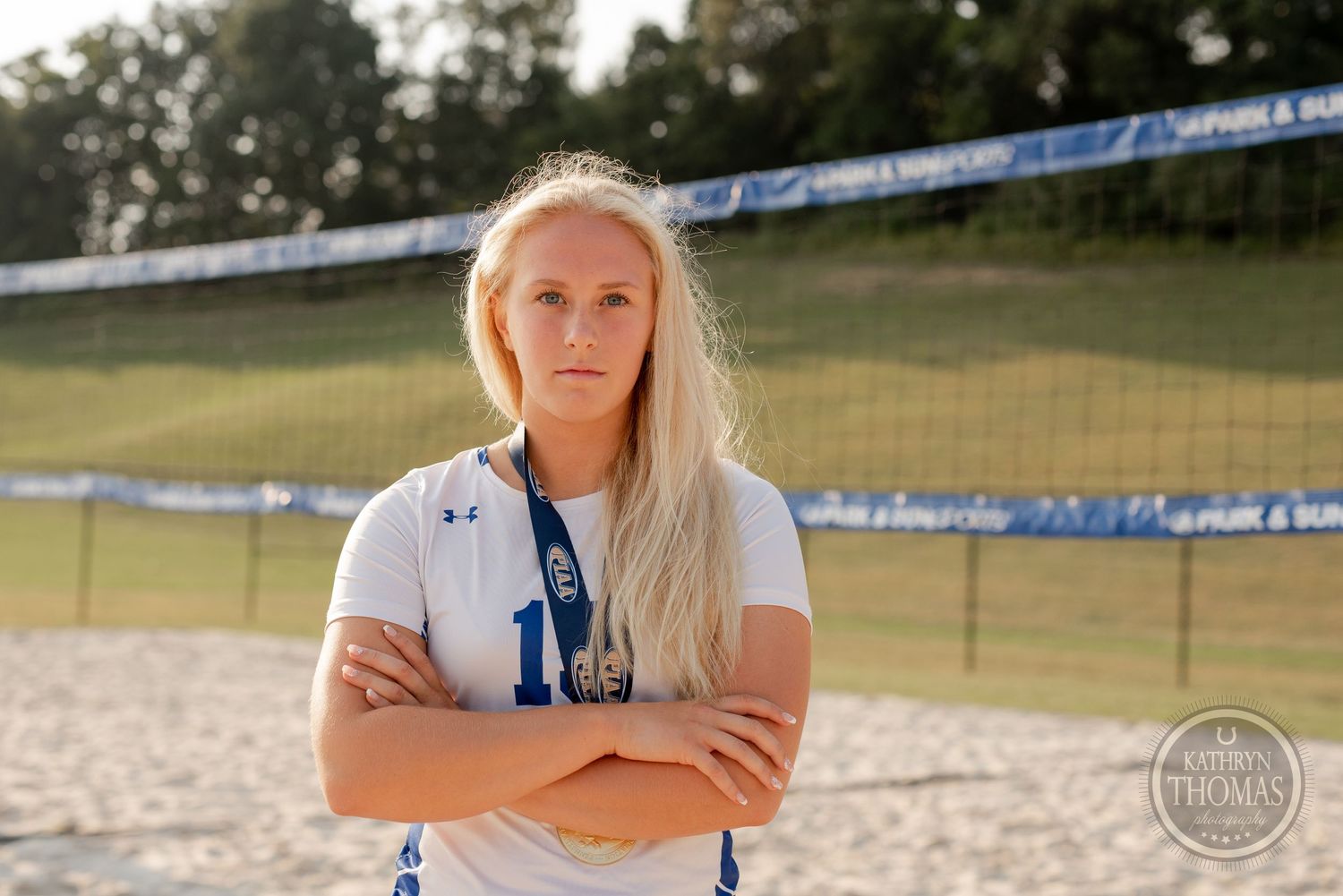 Athlete in Under Armour uniform stands on beach volleyball court with crossed arms.