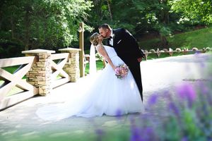 Wedding couple posing in garden setting with purple flowers and white architectural details.