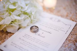 Wedding rings and invitation details with white floral accents photographed on textured paper.