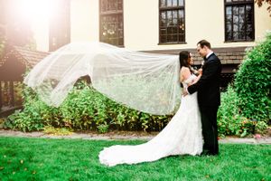 Wedding veil flowing dramatically in the breeze against white building backdrop.