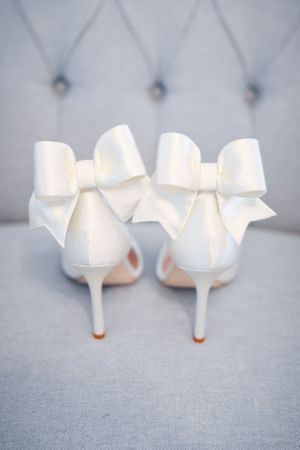 Elegant white bridal shoes photographed from different angles against a grey fabric background.