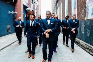 Groomsmen walking and posing casually in navy suits along urban brick alleyway.