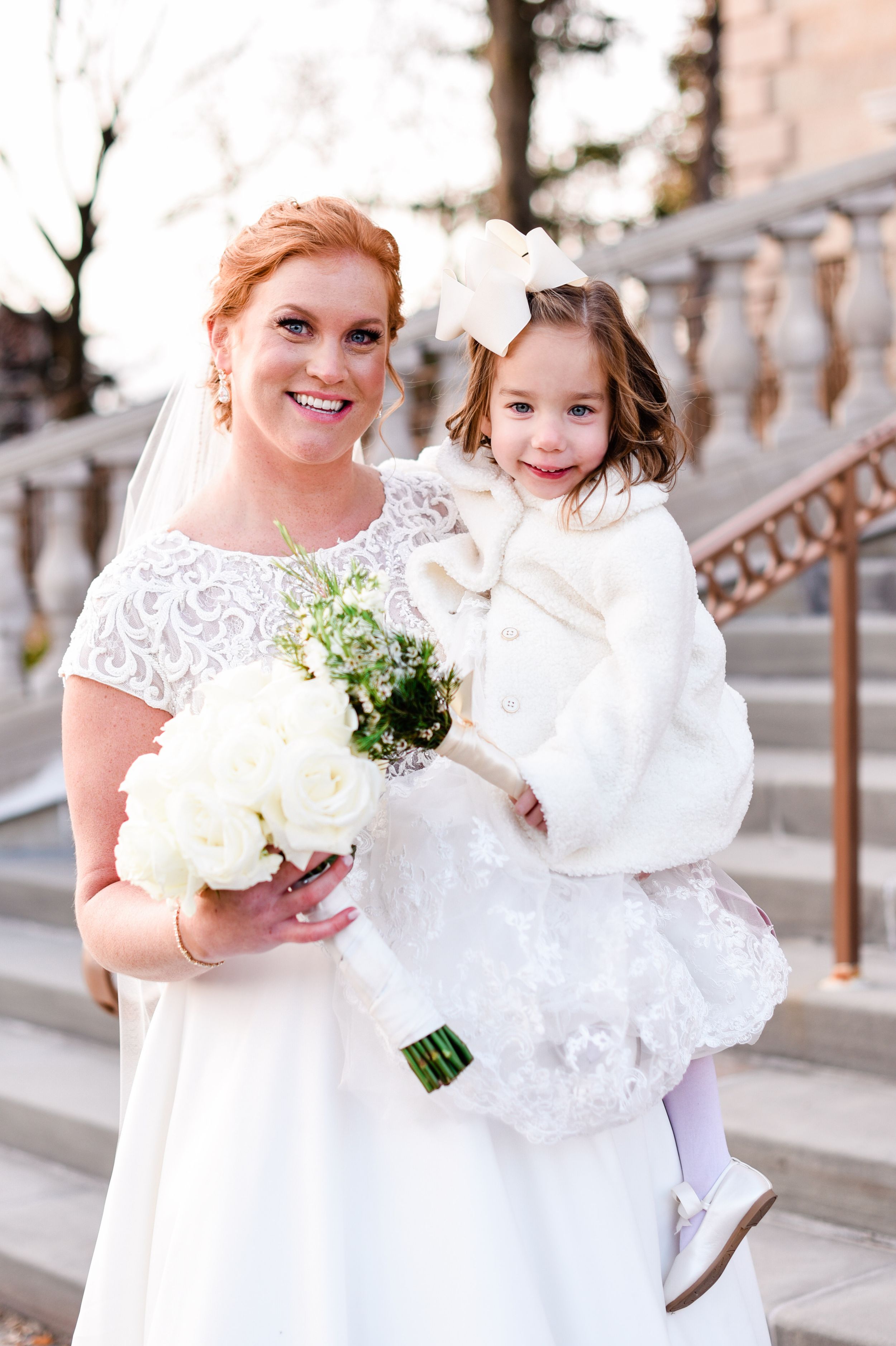A white wedding dress and bouquet shown in elegant detail against a stone architectural backdrop.
